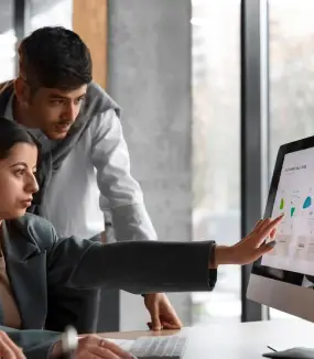 Two marketing professionals reviewing and discussing data graphs on a computer monitor