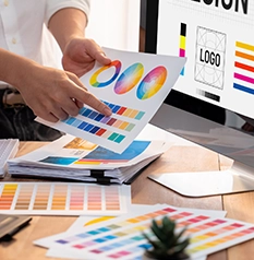 A smartphone displays a web design mockup among various design process papers and tools on a wooden surface.